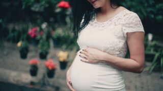 close up photo of pregnant woman in white dress holding her stomach